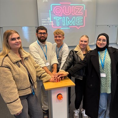 Fünf Personen stehen um einen Quiz-Tisch, ihre Hände auf einem roten Knopf. Im Hintergrund leuchtet ein "QUIZ TIME"-Schild.