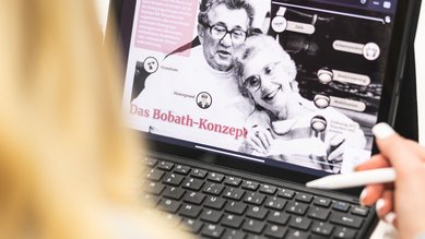 Eine Person betrachtet auf einem Tablet eine Webseite über das Bobath-Konzept, mit Bildern von zwei älteren Menschen und erklärenden Texten.