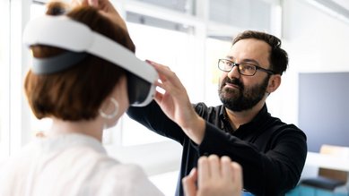 Ein Mann hilft einer Frau, ein Virtual-Reality-Headset aufzusetzen, während sie in einem modernen Raum stehen.