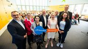 Gruppenshot von Personen, die ein Schild mit der Aufschrift "srh Gesundheit SRH University" halten, vor einem Publikum in einem großen Raum.