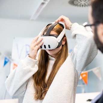 Eine Person mit langen Haaren setzt ein VR-Headset auf und bereitet sich darauf vor, eine virtuelle Realität zu erleben.